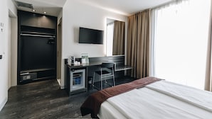 Una habitación de hotel moderna con una cama grande, un escritorio con televisor de pantalla plana, un armario y un minibar.
