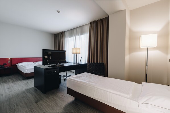 Habitación de hotel con cama, escritorio, silla, televisor, lámpara y cortinas.