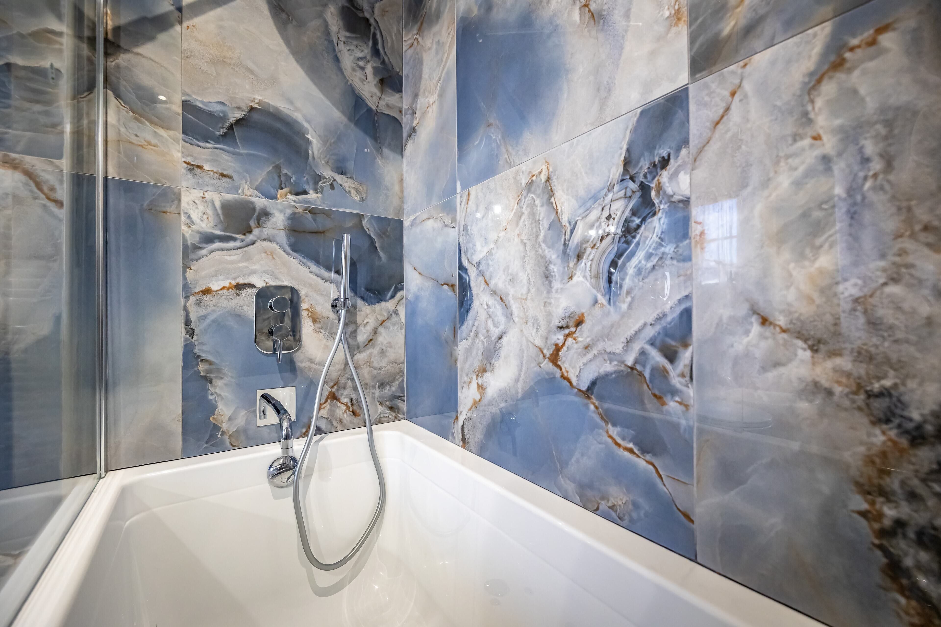 A modern bathroom with a marble backsplash and a white bathtub.
