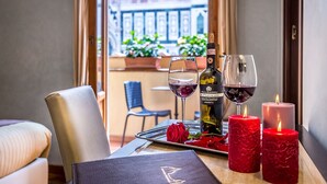 Una mesa puesta con una botella de vino, dos copas de vino, velas rojas y una rosa.