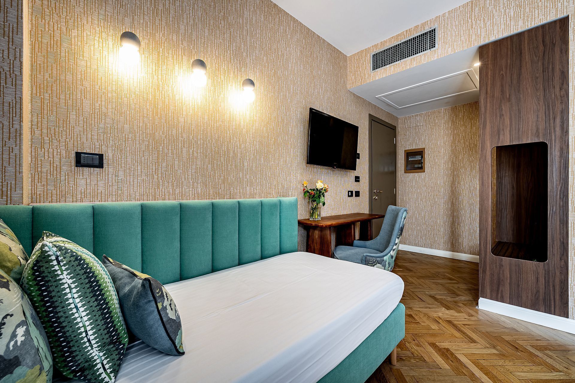 A modern hotel room with a green sofa, a wooden desk, and a flat-screen TV mounted on the wall.