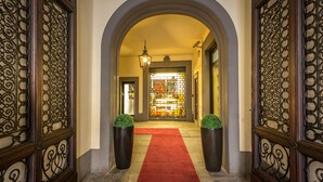 Un pasillo con alfombra roja, puertas de metal ornamentadas y un candelabro.