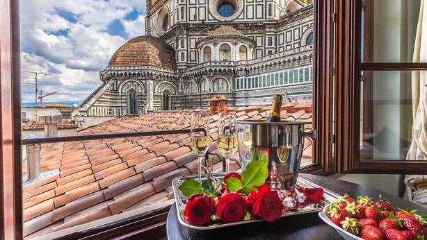 Vista de la Catedral de Florencia desde una ventana, con una botella de champán y un bol de fresas sobre la mesa.