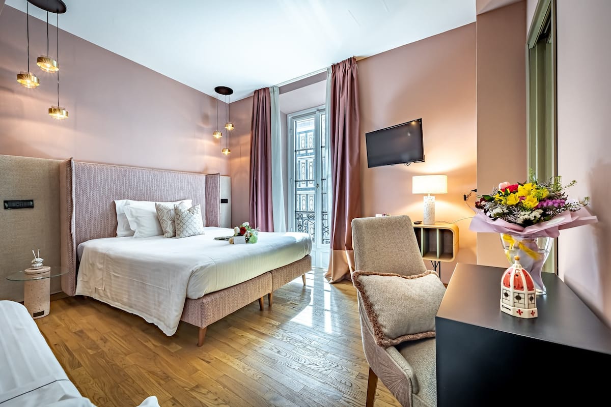 Habitación de hotel con una cama grande, una silla, un televisor y un escritorio con un florero.