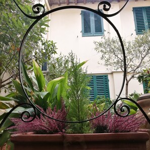 A courtyard with potted plants and a building with blue shutters. - Aurum Uffizi (Florence)