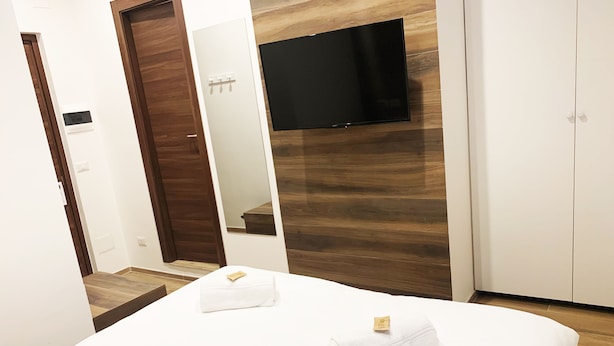Habitación de hotel con cama, televisor de pantalla plana montado en la pared, armario de madera y espejo.