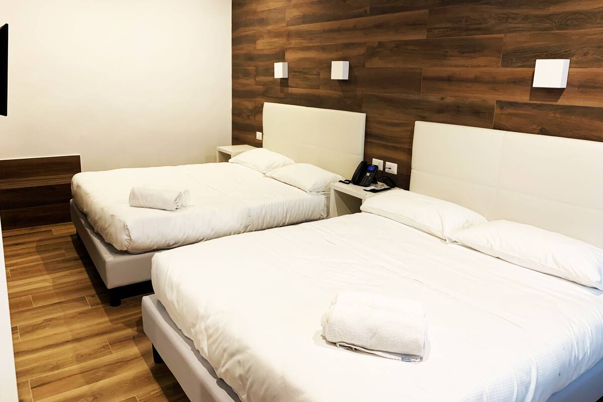 A hotel room with two beds, wooden flooring, white walls, and a wooden accent wall.