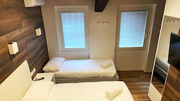 Habitación de hotel con dos camas, suelo de madera, televisor y ventanas con persianas.