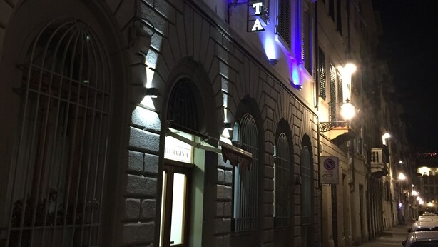 A hotel facade with illuminated signage, arched windows, and a narrow street. - Hotel Magenta (Florence)