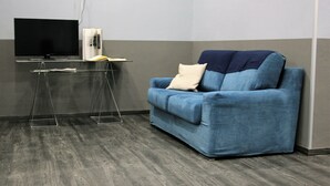 A room with a blue sofa, a flat-screen TV, a small table with a book and a remote, and a grey carpeted floor. - Hotel Magenta (Florence)