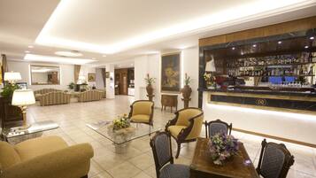 A hotel lobby with a bar area, seating arrangements, and a reception desk.