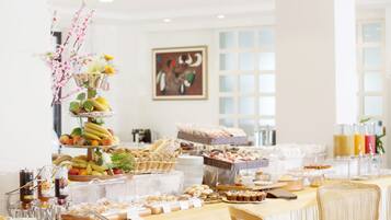 Una mesa de buffet con diversos alimentos y bebidas, un arreglo floral decorativo y una obra de arte enmarcada en la pared.