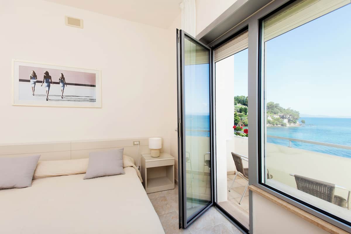 Une chambre d’hôtel comprenant un lit, une table de chevet, une chaise et une grande fenêtre donnant sur la mer.