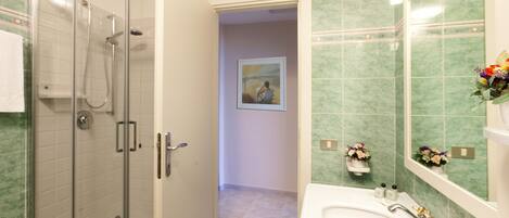A bathroom with a glass-enclosed shower, a white sink with gold fixtures, and green-tiled walls.