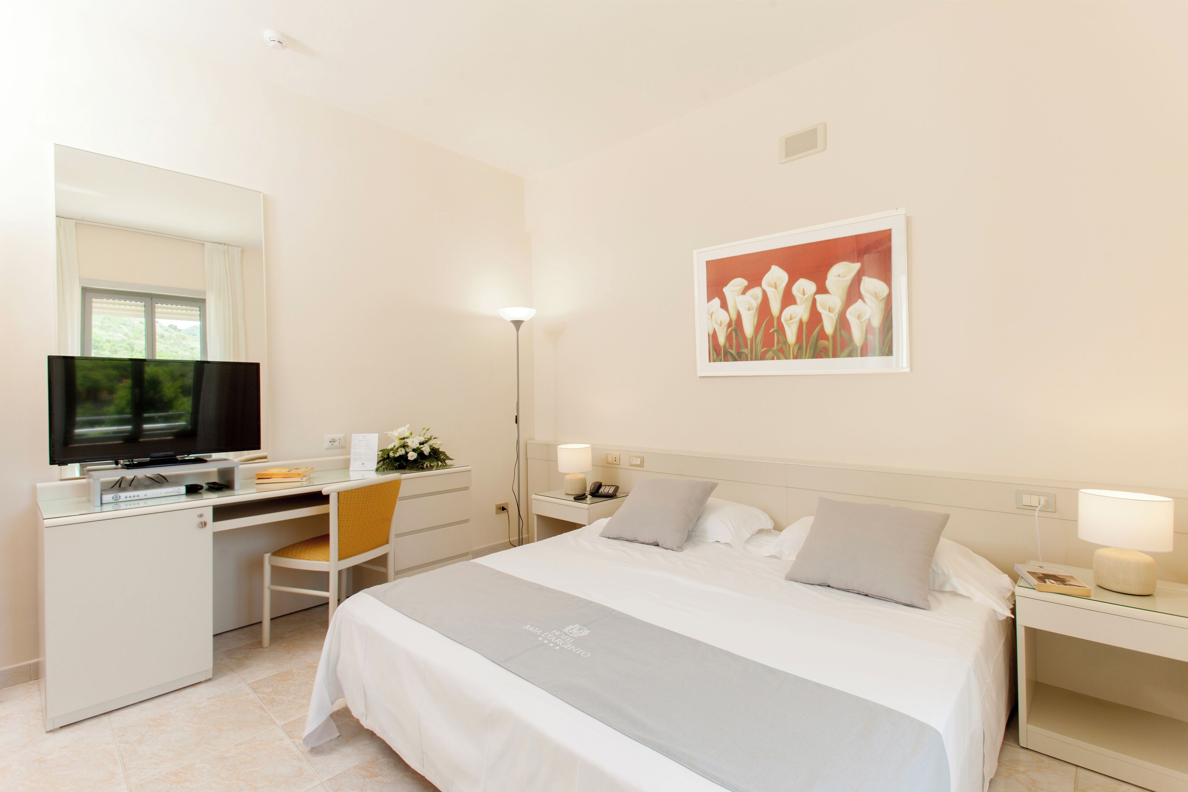 Ein Hotelzimmer mit Bett, Schreibtisch mit Fernseher, Stuhl, Nachttisch und Wandbild.