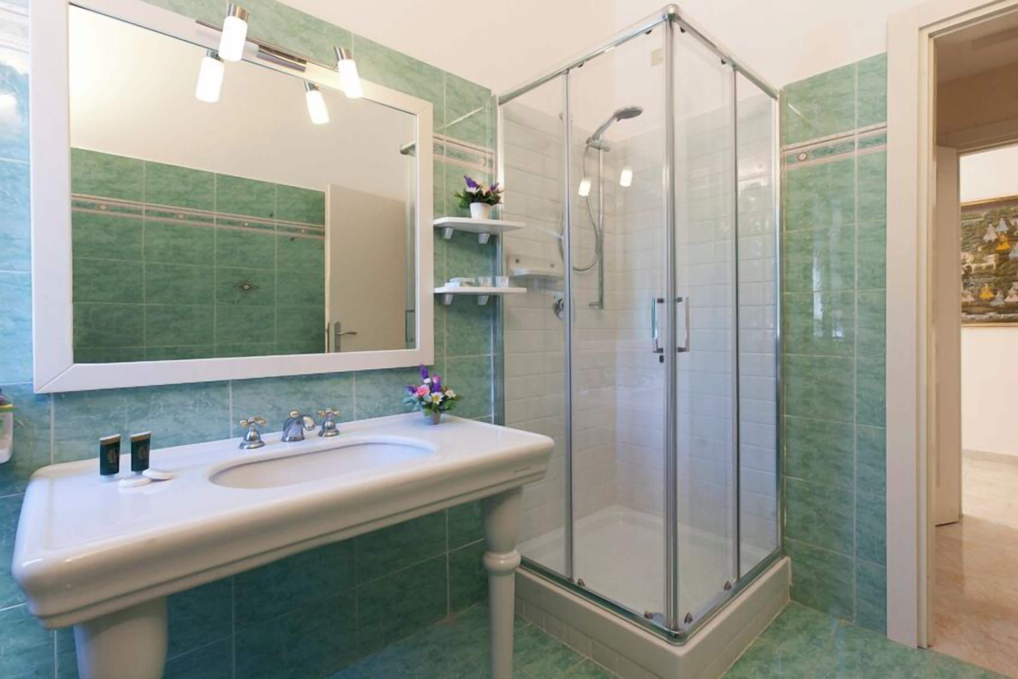 A bathroom with a white sink, a glass-enclosed shower, and green-tiled walls.