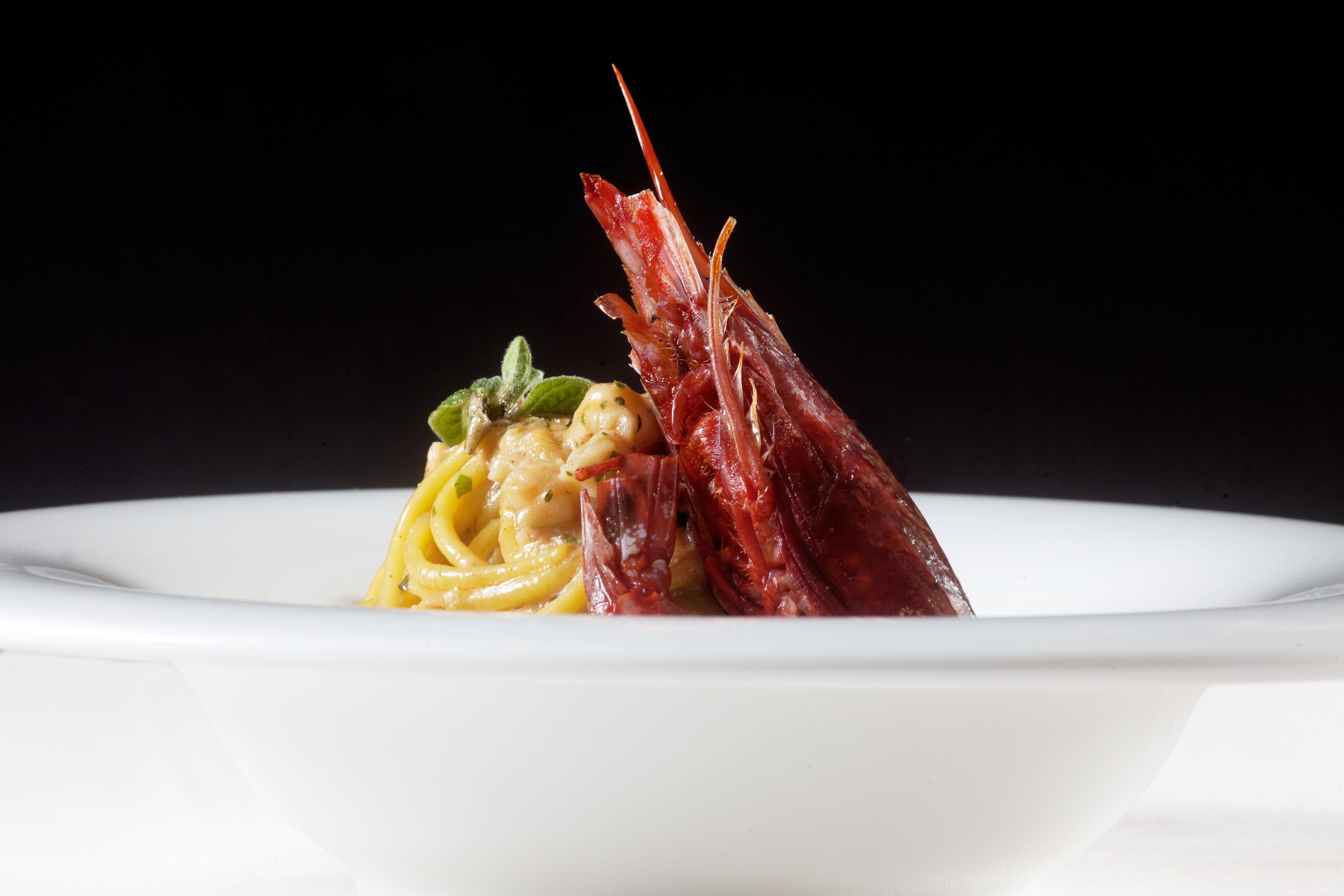 Un piatto bianco con pasta e una coda di aragosta rossa.