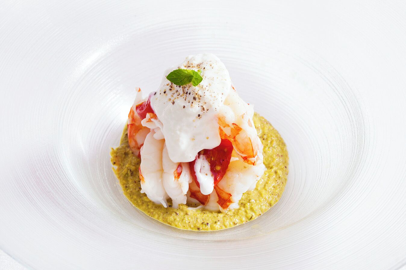 Un plat composé de crevettes, d’une sauce blanche et d’une garniture verte, le tout servi dans une assiette blanche.