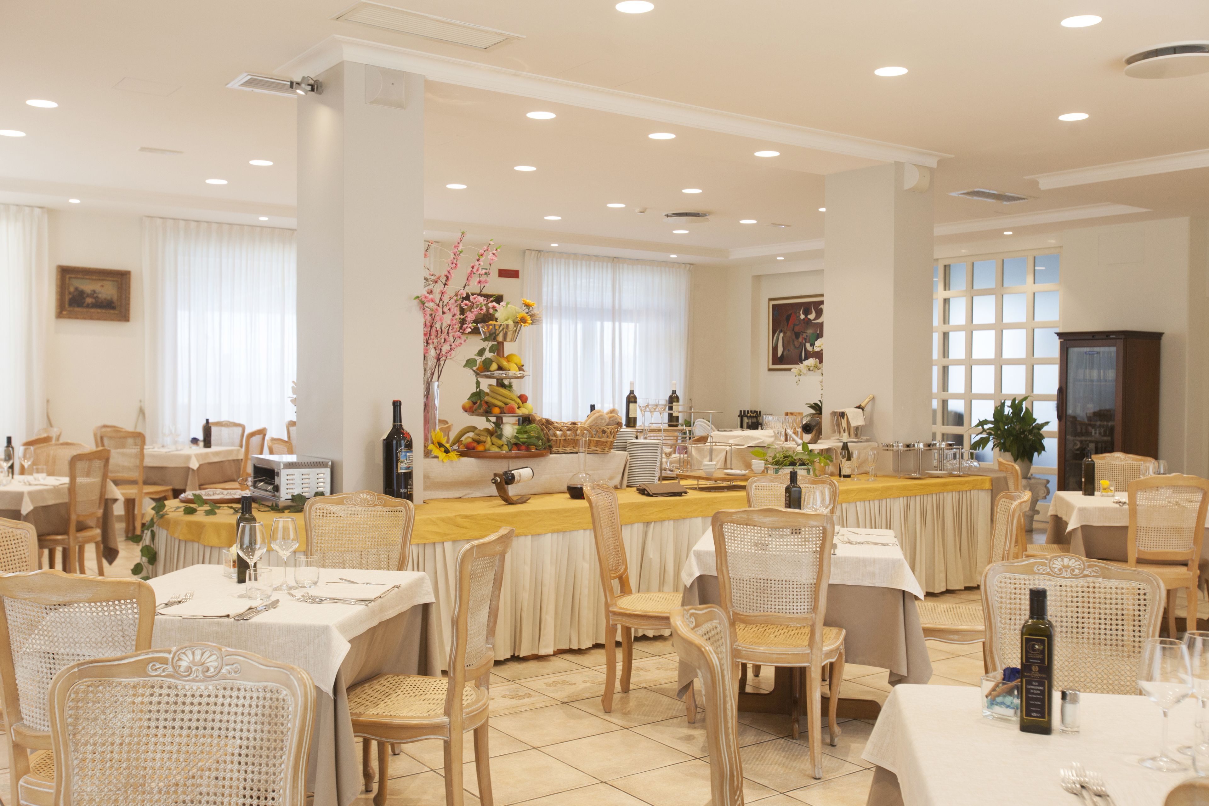A spacious dining area with multiple tables and chairs, a central bar area with a variety of food and drink items, and large windows allowing natural light.