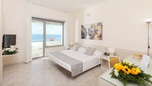 A hotel room with a bed, a desk with a telephone, a chair, a desk lamp, and a view of the sea through a sliding door. - Baia d'Argento (Monte Argentario)