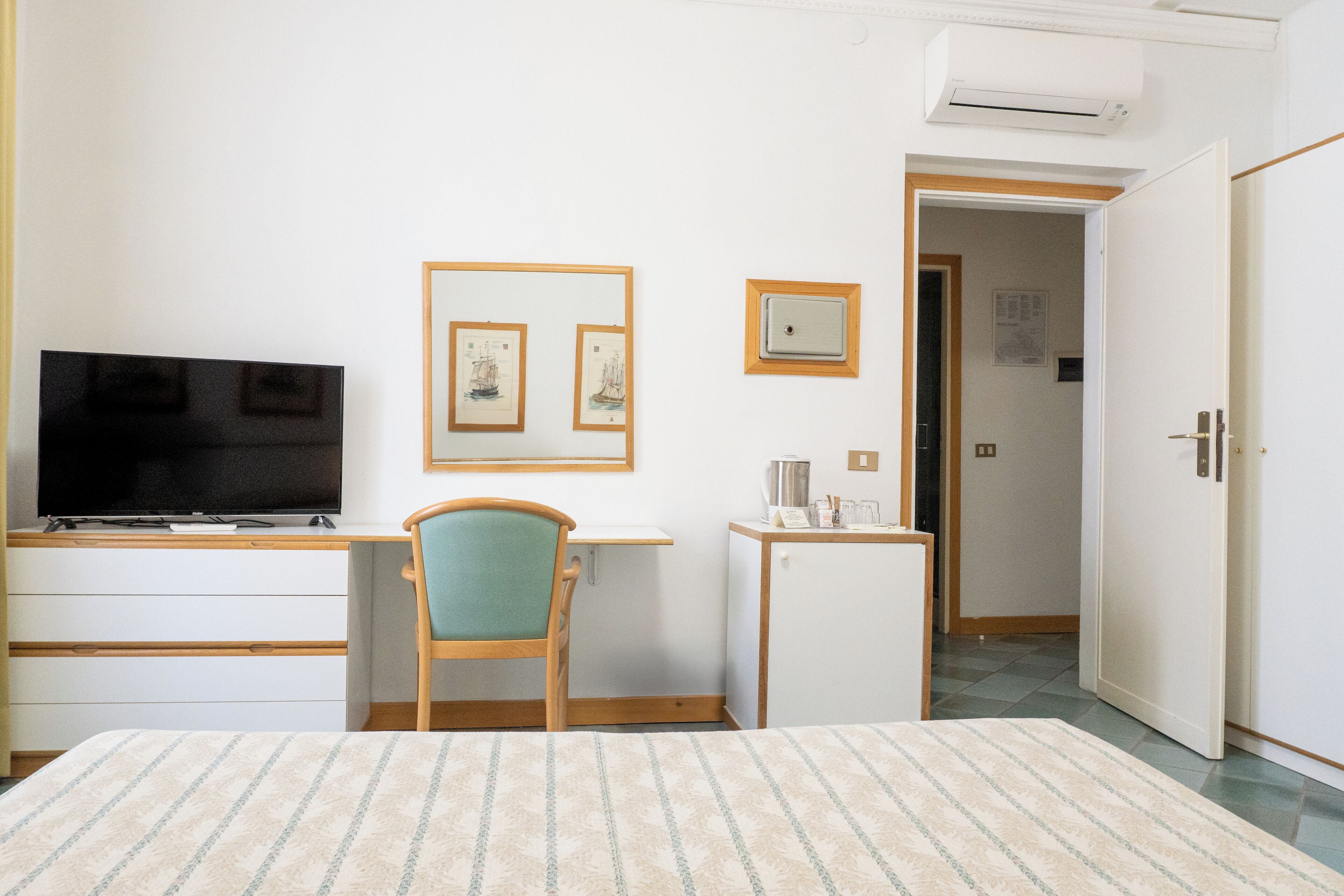 Ett hotellrum med en säng, ett skrivbord med en dator, en stol, ett litet bord med en vattenkokare och inramade tavlor på väggen.