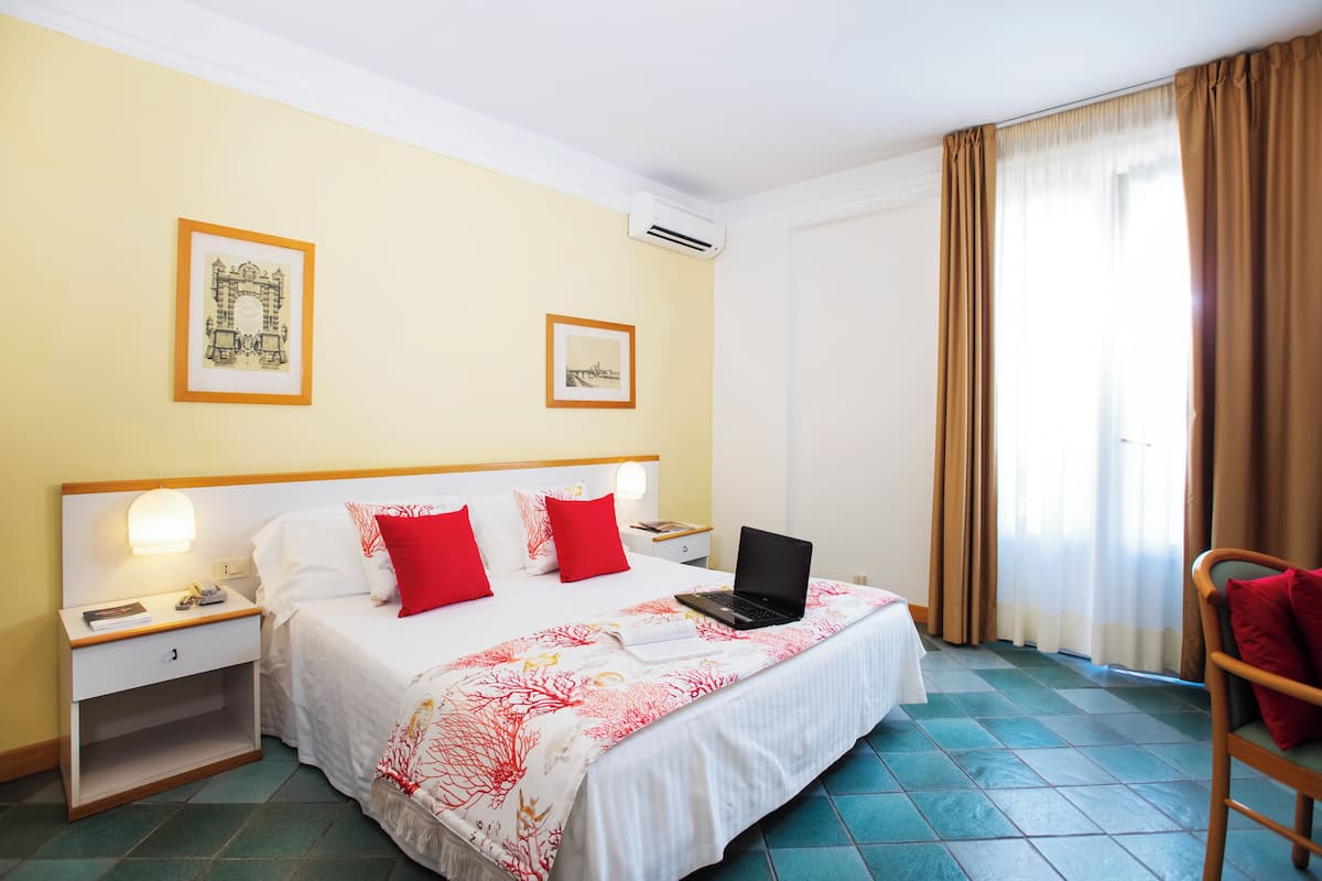 A hotel room with a bed, a desk, a chair, and two framed pictures on the wall.