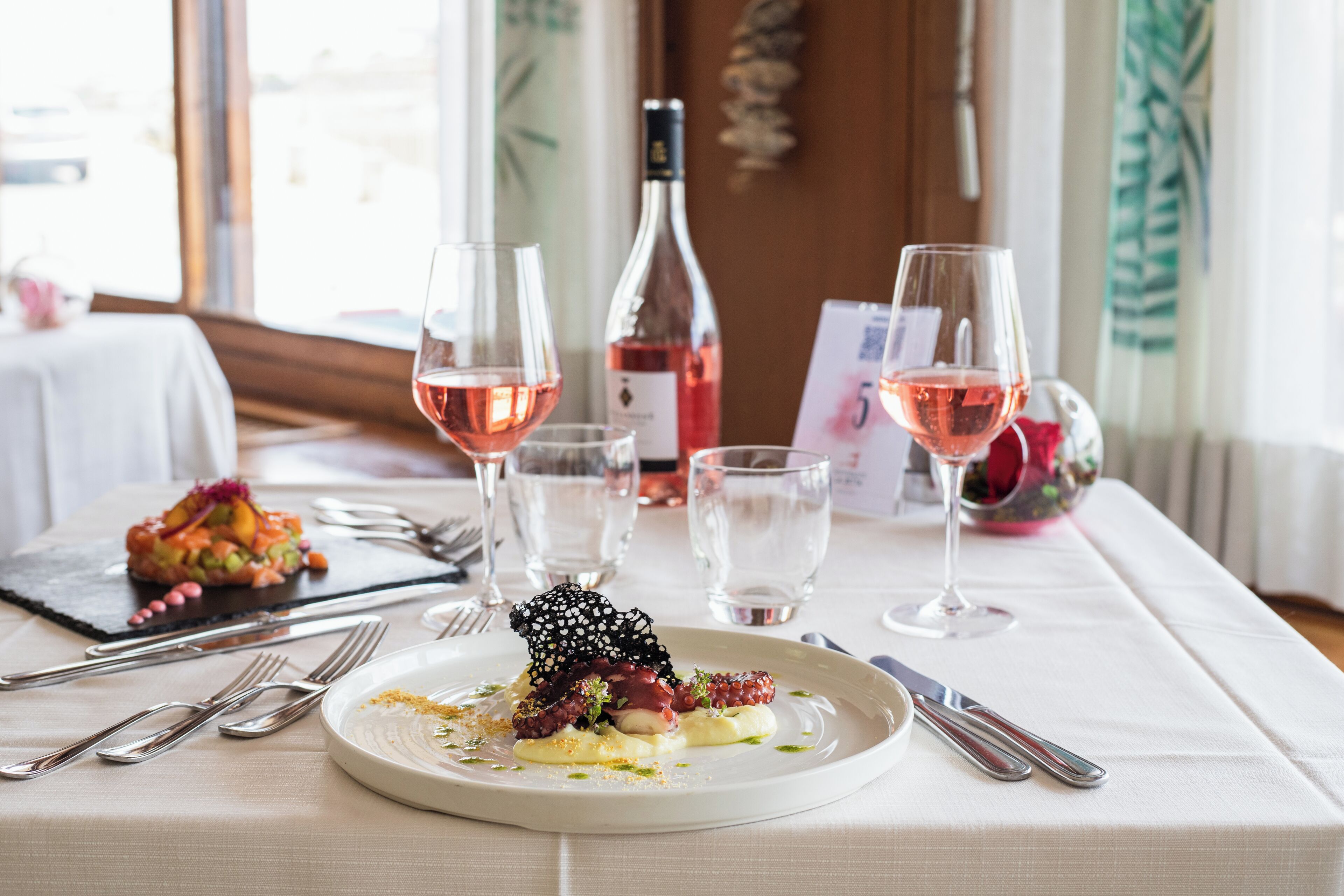 A dining table with a white tablecloth, a plate of food, wine glasses, and a wine bottle.