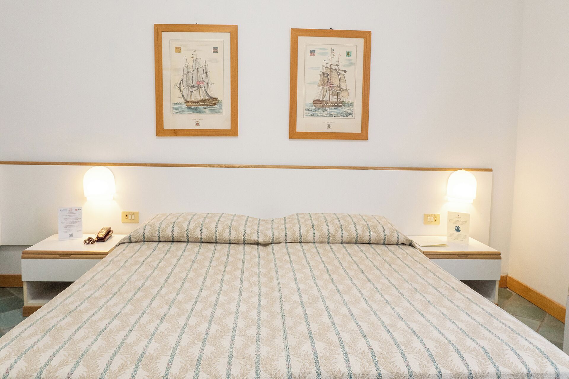 A neatly made bed with a patterned bedspread, two bedside tables with lamps, and two framed pictures on the wall.