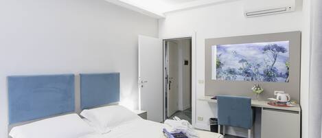 A hotel room with a bed, a desk, a chair, a painting, and an air conditioning unit.