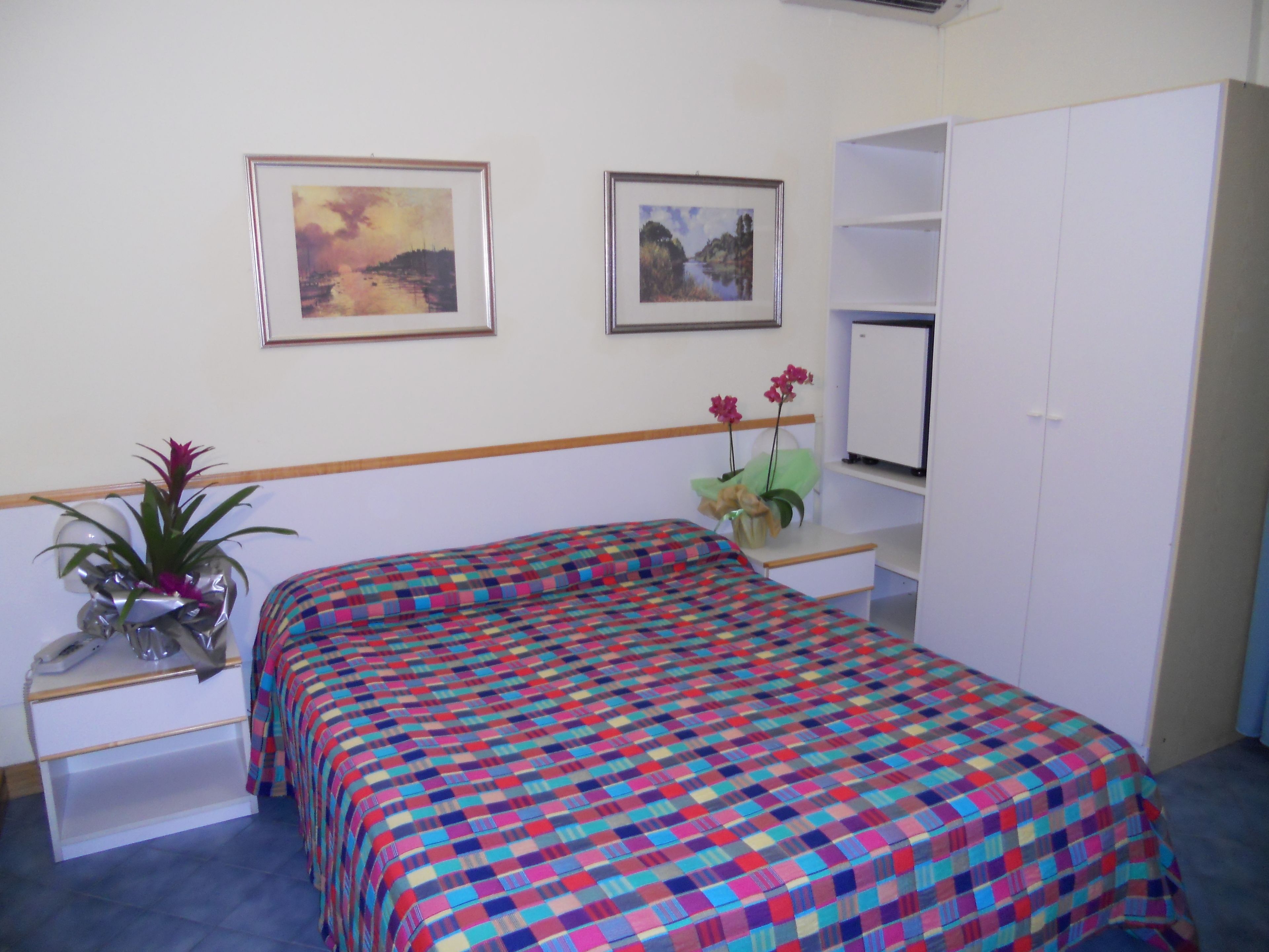 Une chambre à coucher comprenant un lit, un bureau, une chaise, une armoire, une plante et deux tableaux encadrés accrochés au mur.