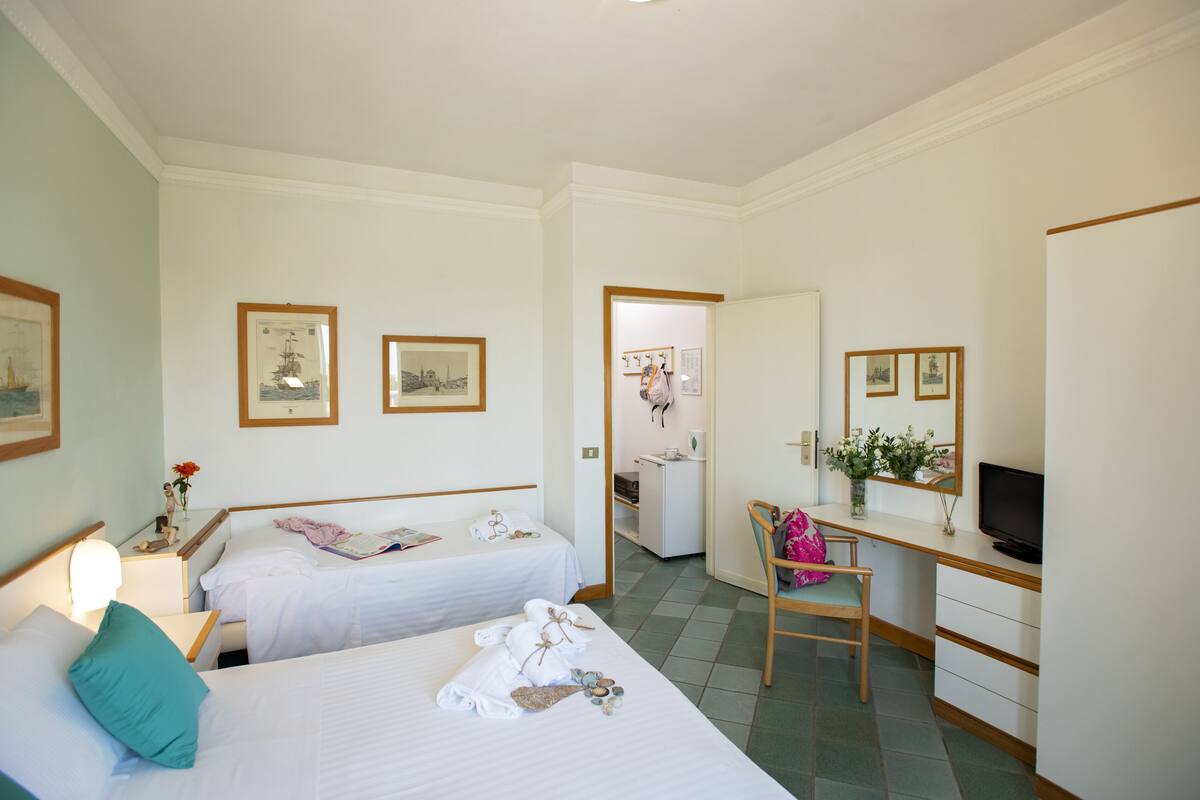 A hotel room with two beds, a desk, a TV, and a bathroom visible through an open door.