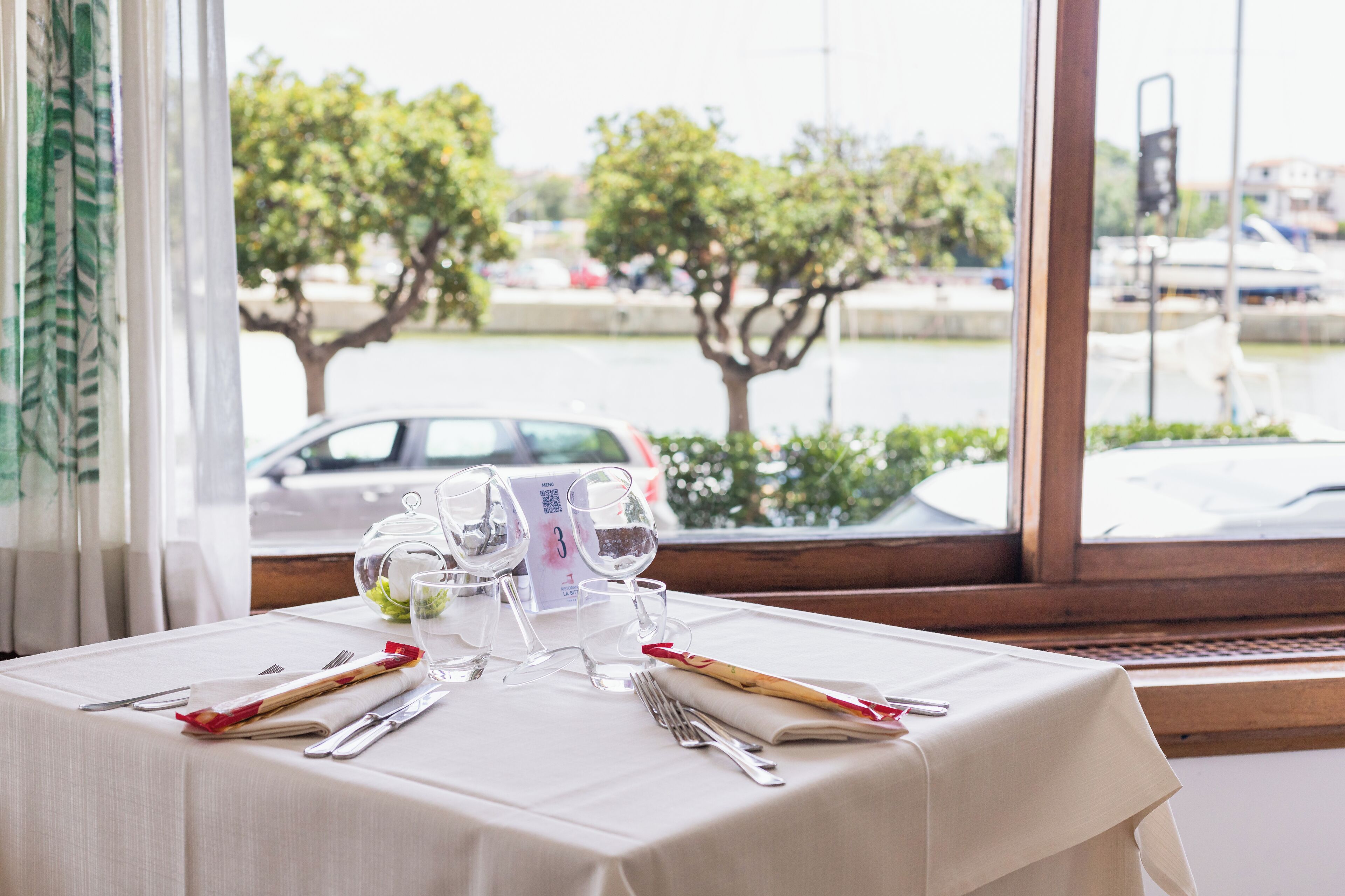 A table set for dining with a view of a marina and trees.