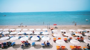 Ein Strand mit Liegestühlen und Sonnenschirmen, bewölkter Himmel und ruhigem Meer.