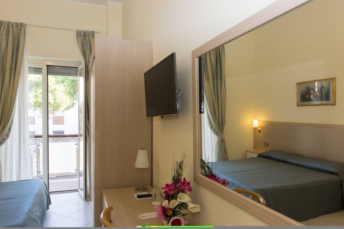 A hotel room with a bed, a TV, a desk with a lamp, and a window with curtains.