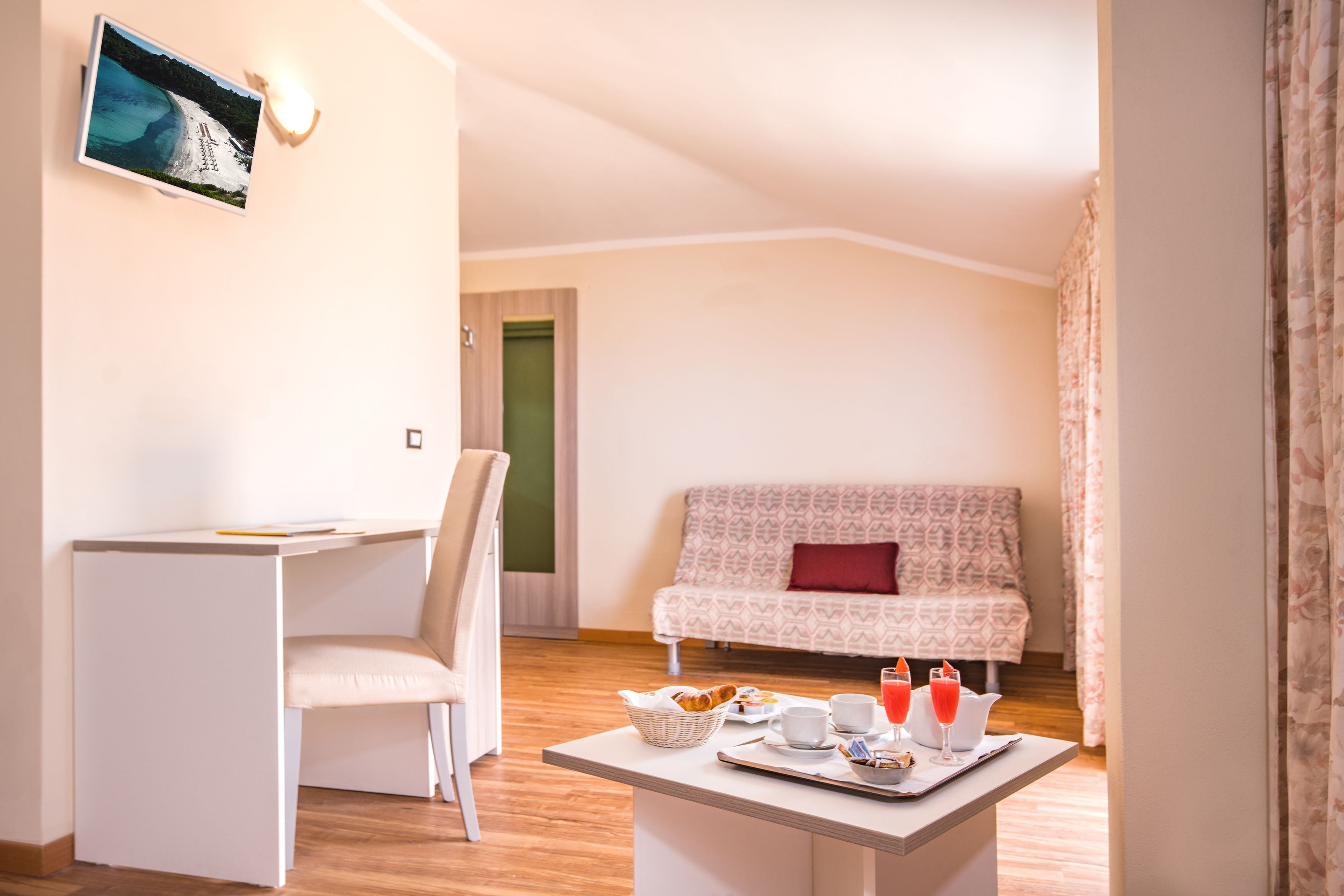 Ein Zimmer mit Schreibtisch, Stuhl, Sofa und einem Frühstückswagen mit Croissants, Kaffeetassen und Saftgläsern.