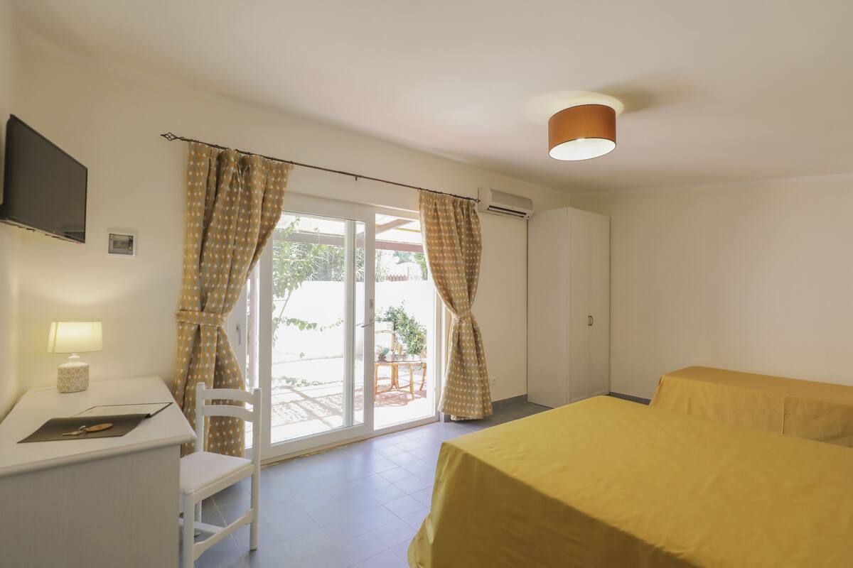 A hotel room with a bed, a desk with a lamp, a chair, and a TV.