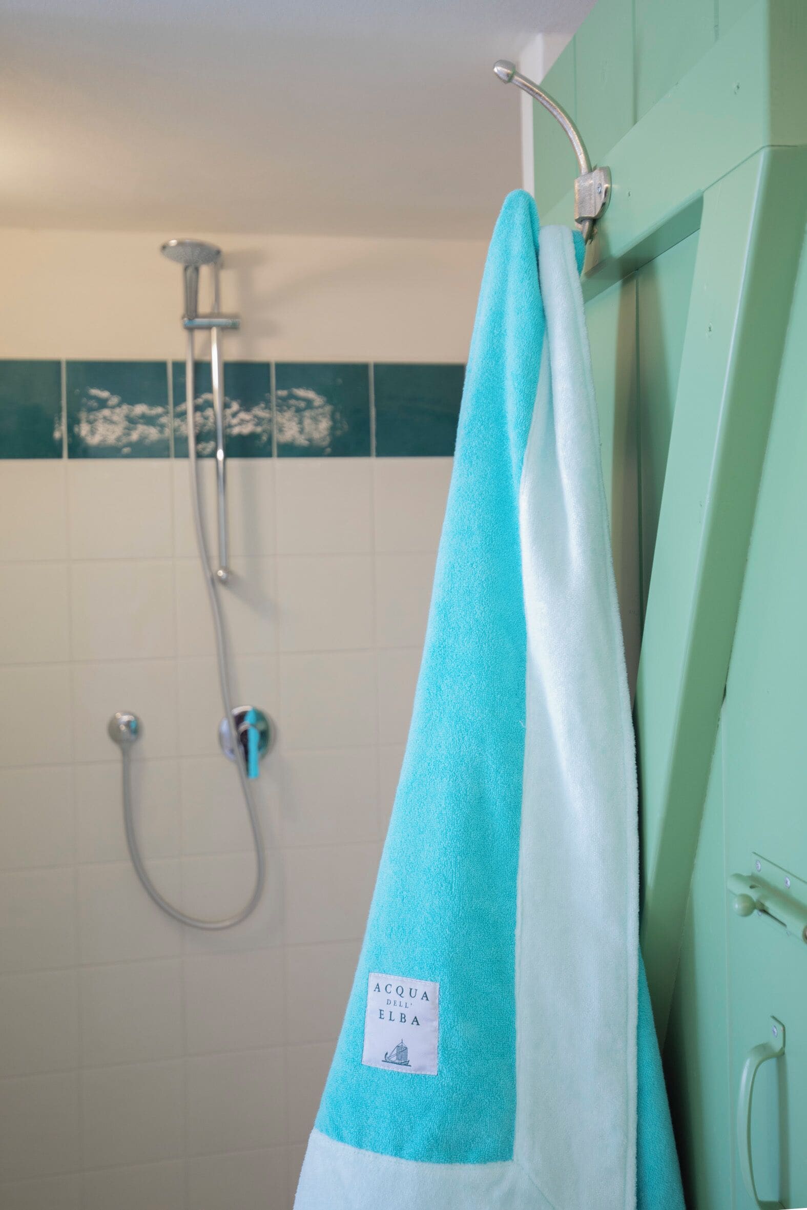 Un baño con ducha, una toalla colgada en un perchero y una pared verde.
