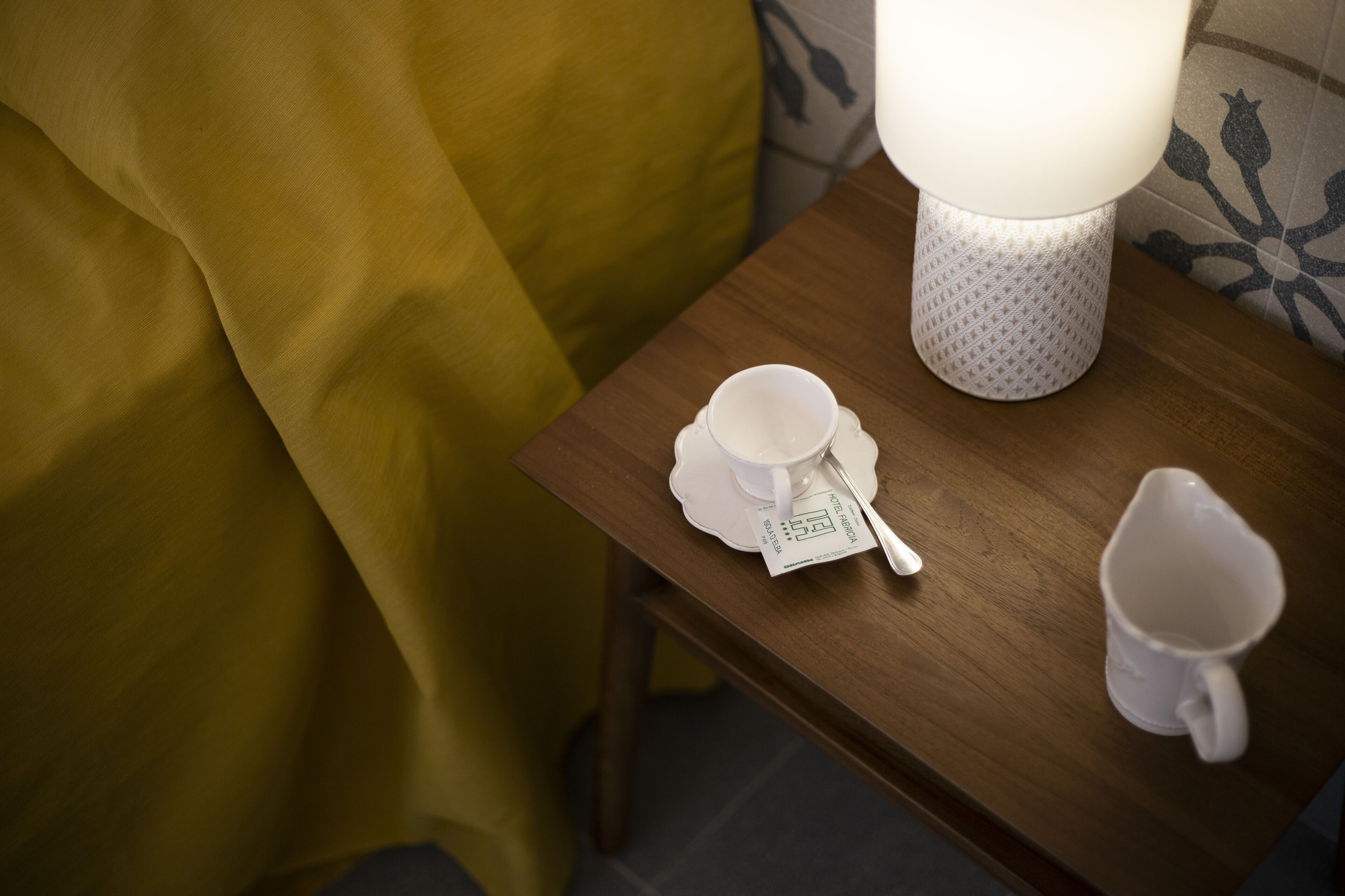 Une table en bois sur laquelle se trouvent une tasse blanche, une soucoupe et un petit objet blanc portant une inscription.