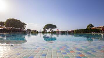 Uma piscina com piso azulejado, rodeada por guarda-sóis e árvores.