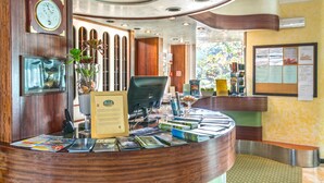 A reception desk with a clock, computer, and various informational materials. - Hotel Fabricia (Portoferraio)
