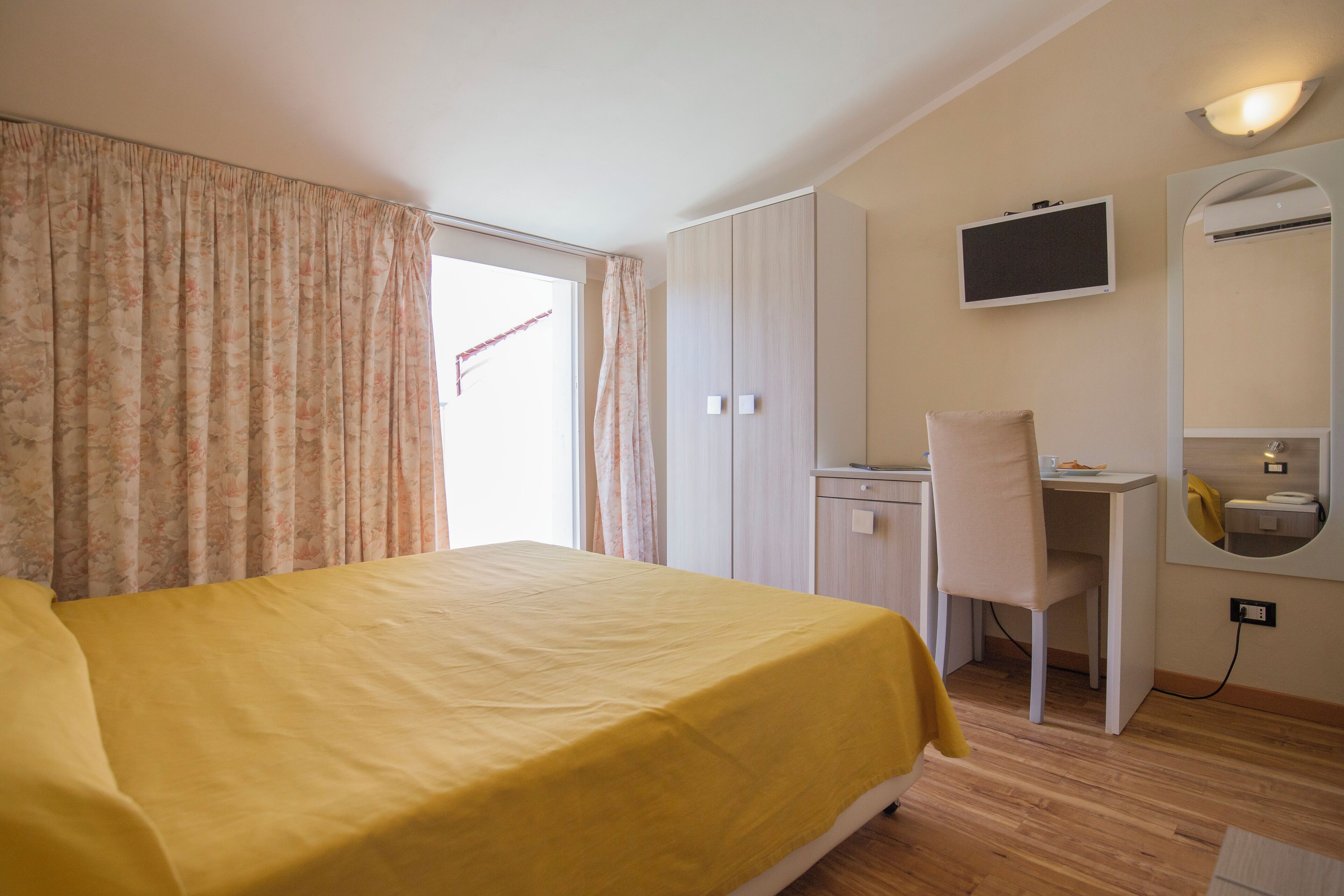 Habitación de hotel con cama, escritorio, silla, televisor y espejo.