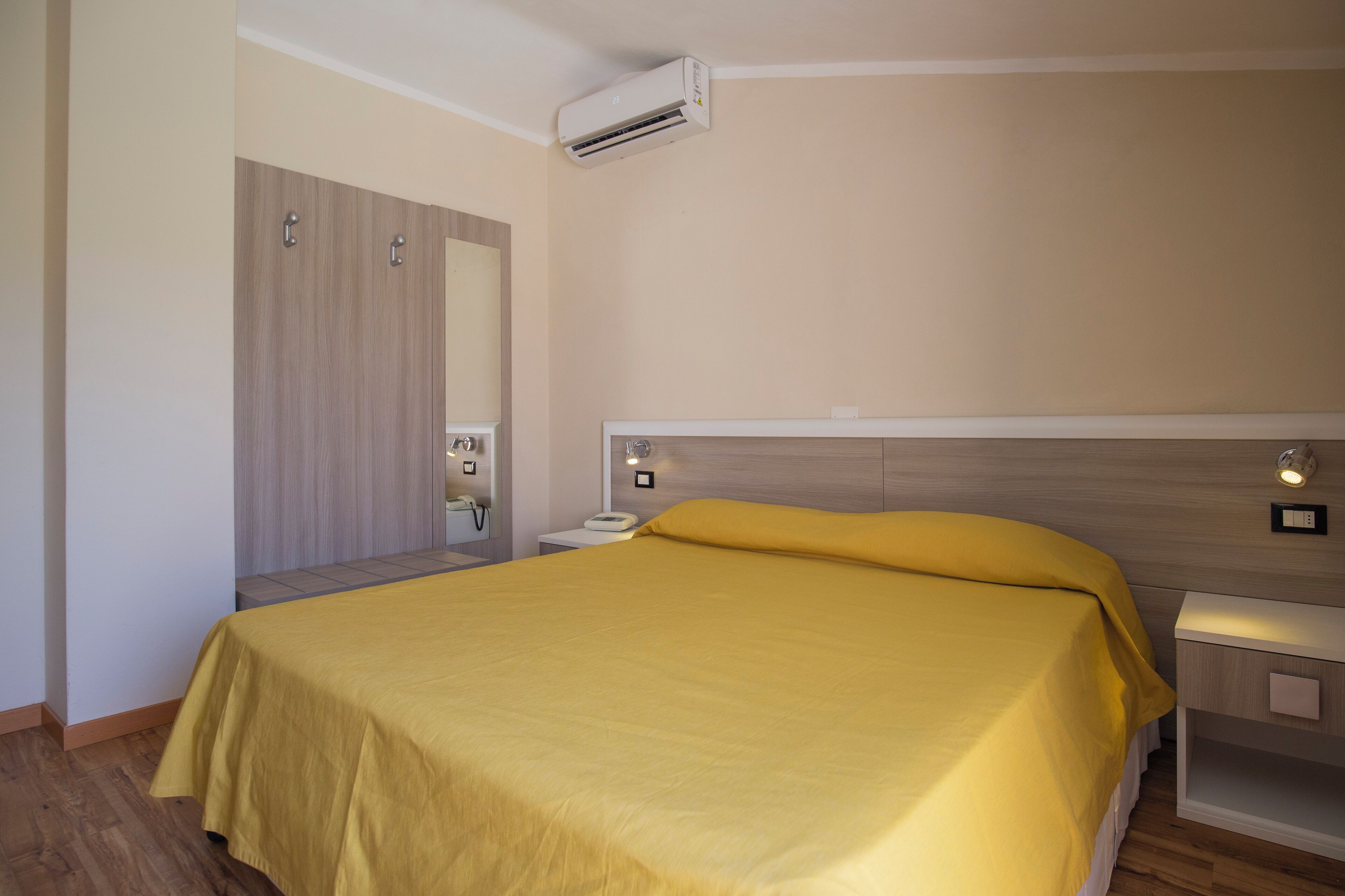 Een hotelkamer met een bed, nachtkastje, spiegel en een airconditioning.