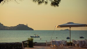 A seaside restaurant with outdoor seating, tables, and umbrellas, overlooking calm waters and a distant island. - Hotel Fabricia (Portoferraio)