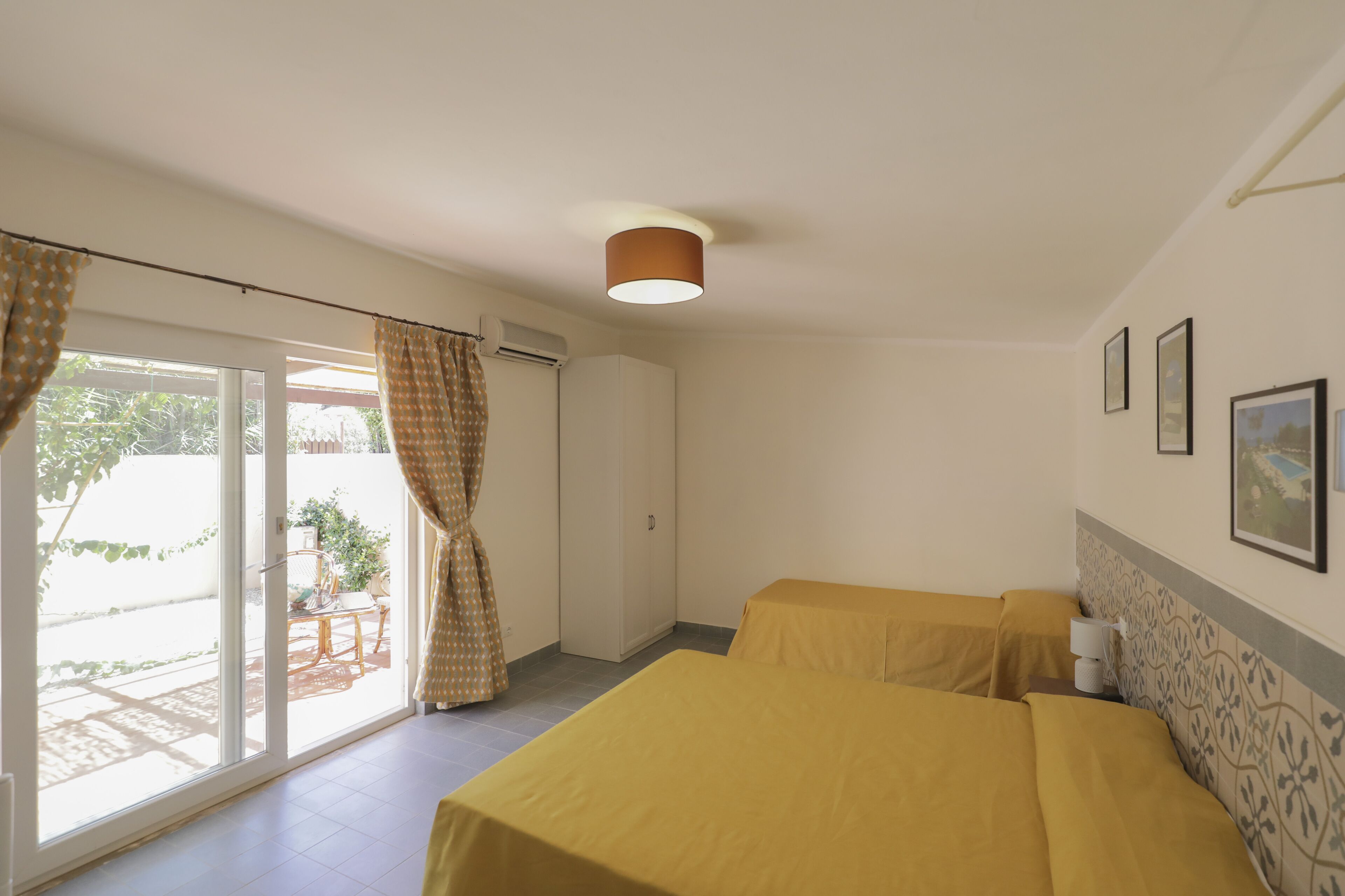 A hotel room with two beds, a ceiling lamp, a window with curtains, and a wall-mounted picture.