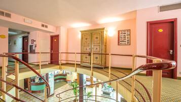Een hotellobby met meerdere niveaus, een centrale trap, een receptiebalie en een decor kast.