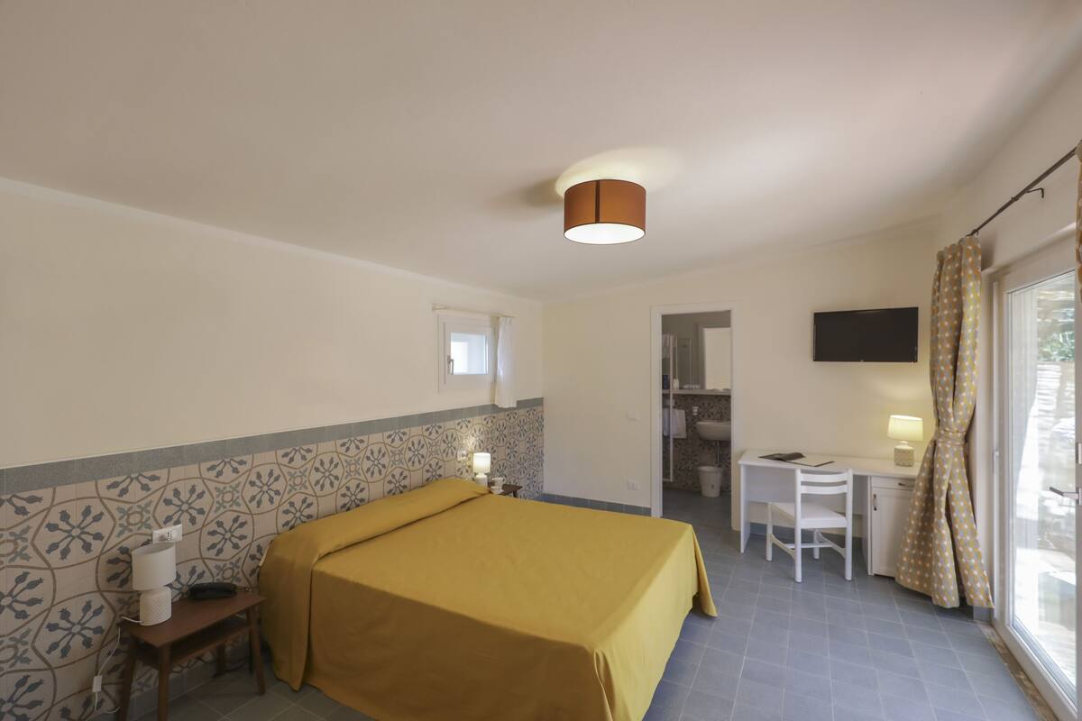 A hotel room with a bed, a desk, a chair, a television, and a bathroom visible through an open door.