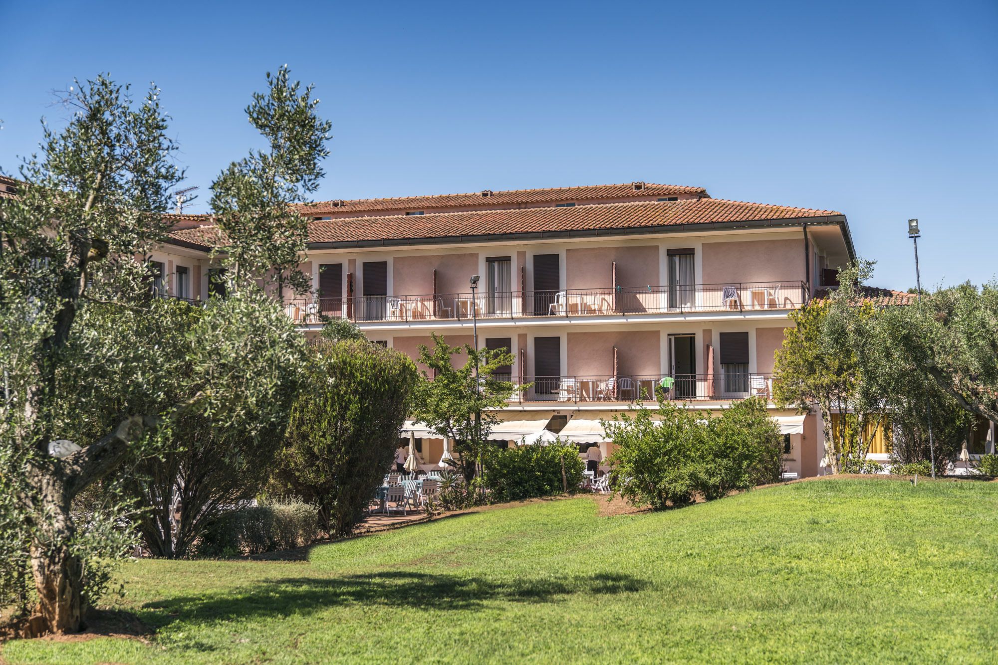 Um edifício com vários andares e varandas, rodeado por vegetação e um gramado bem cuidado.