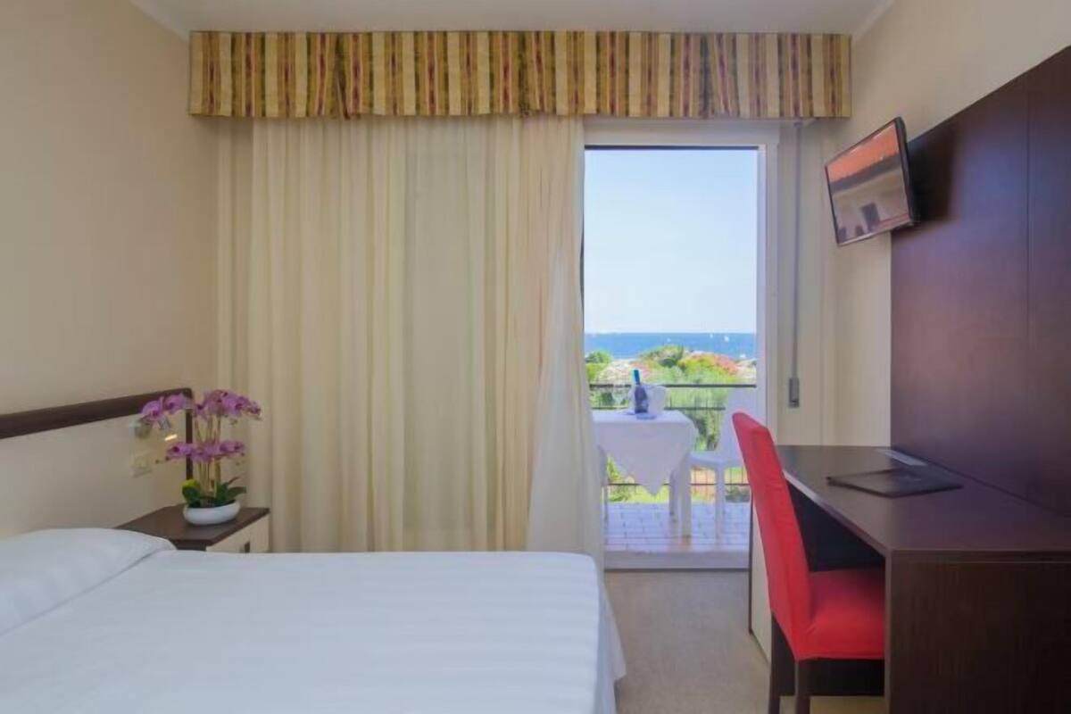 A hotel room with a bed, a desk, a chair, a TV, and a view of the outdoors.