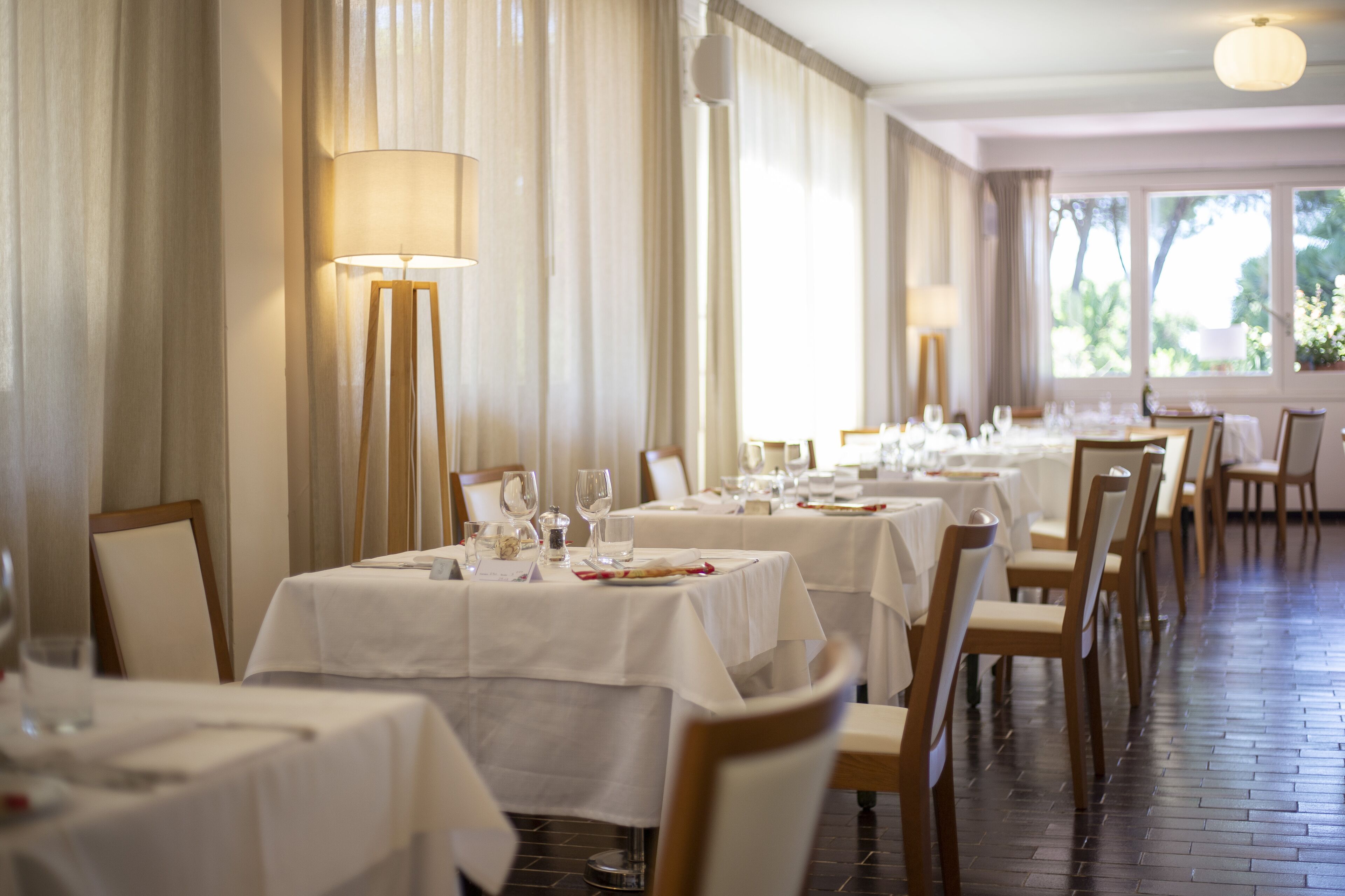 A restaurant with multiple tables, each covered with white tablecloths, and chairs with wooden frames and white cushions.