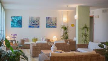 A cozy lounge area with wicker furniture, wall-mounted artwork, and potted plants.